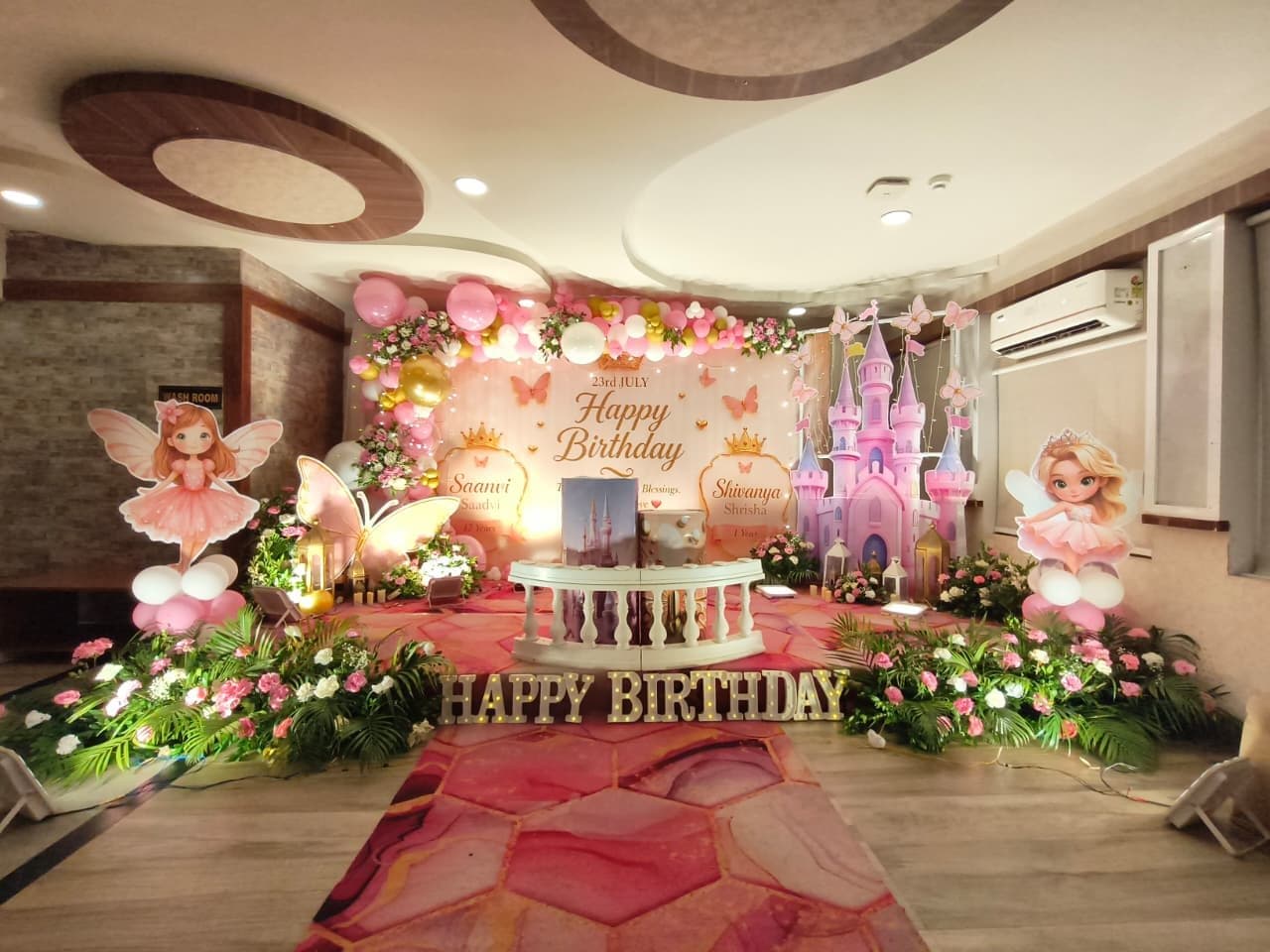 Pink and gold fairy princess birthday stage with a castle backdrop, fairy cutouts and Happy Birthday marquee letters